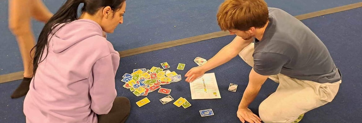Two adults sitting on the floor looking at cards that tell them what next for conditioning exercises 