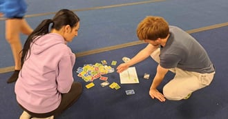 Two adults sitting on the floor looking at cards that tell them what next for conditioning exercises 